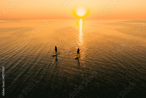 Photos Aerial view of two people on stand up paddle boards on quiet sea at sunset