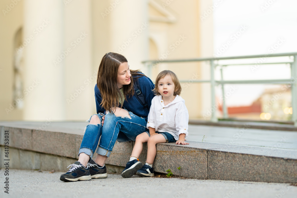 Cute funny toddler boy in his mothers arms. Mom and son having fun on sunny autumn day in a park.