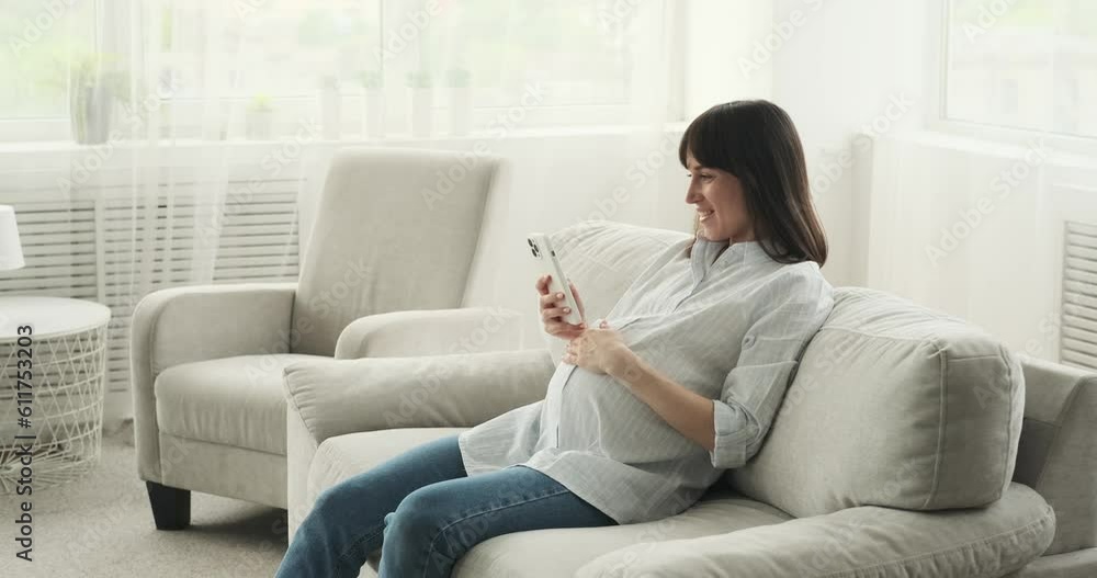 A pregnant woman finding joy in the comfort of her living room. Seated on the couch, she happily engages with her phone, her radiant smile illuminating the space. A pregnant woman finding joy in the comfort of her living room. Seated on the couch, she happily engages with her phone, her radiant smile illuminating the space.