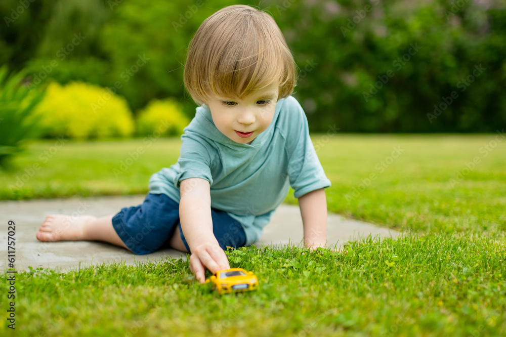 Cute toddler boy playing with yellow toy car outdoors. Kid exploring nature. Small child having fun with toys. Cute toddler boy playing with yellow toy car outdoors. Kid exploring nature. Small child having fun with toys.