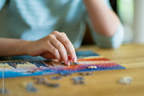 Close-up on woman hand playing puzzles at home. Connecting jigsaw puzzle pieces in a living room table, assembling a jigsaw puzzle.