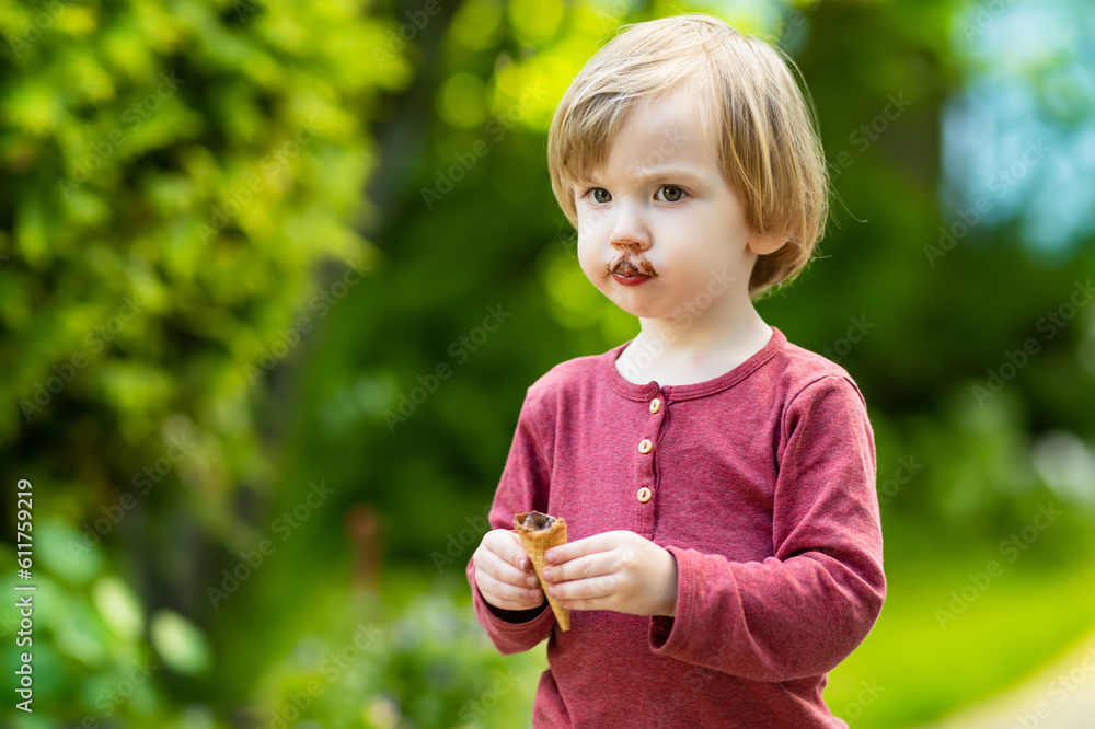 Cute toddler boy eating tasty fresh ice cream outdoors on warm sunny summer day. Children eating sweets. Cute toddler boy eating tasty fresh ice cream outdoors on warm sunny summer day. Children eating sweets.