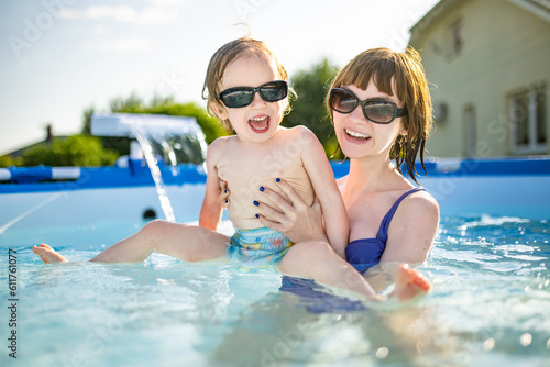 Cuty funny toddler boy and his teenage sister having fun in outdoor pool. Child learning to swim. Kid having fun with water toys. Summer activities for the family with kids.