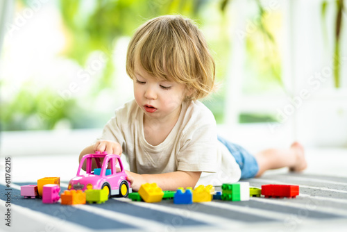 Cute toddler boy playing with blocks construction toy set on the floor at home. Daytime care creative activity. Kids having fun with toys. Educational learning games.