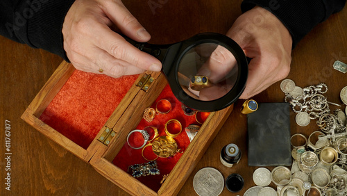 Obraz na płótnie the jeweler, through magnifying glass, examines a ring with a diamond, against the background of a brown table on which precious things lie: rings, pendants, coins made of gold and silver