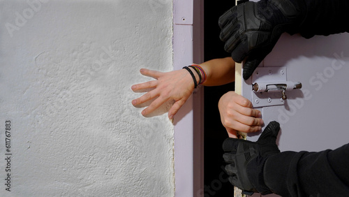 the girl's hands, between the wall and the prison door, which a man in gloves is trying to close.
concept: woman trying to break out of prison. imprisonment. woman in captivity          