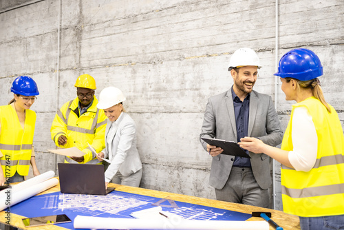 Team of experienced architects and civil engineers analyzing and looking at building plant at construction site.