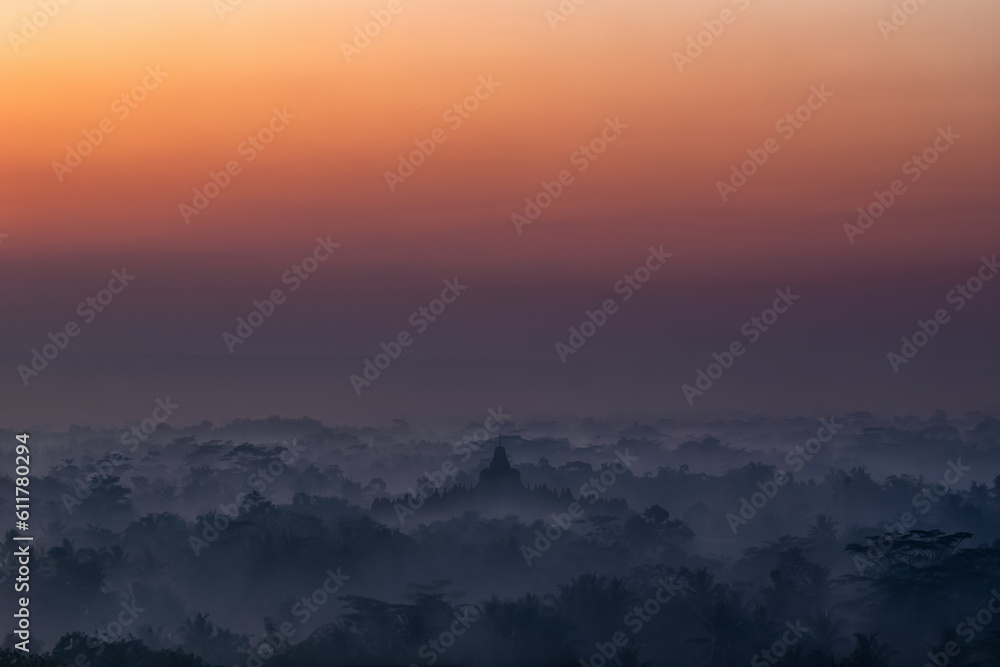 Borobudur Temple complex during sunrise in the middle of misty woods 