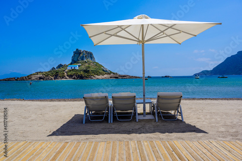 Deck chair and umbrella on beautiful Agios Stefanos Beach in front of paradise Island Kastri- historical ruins and paradise scenery at coast of island Kos  Greece