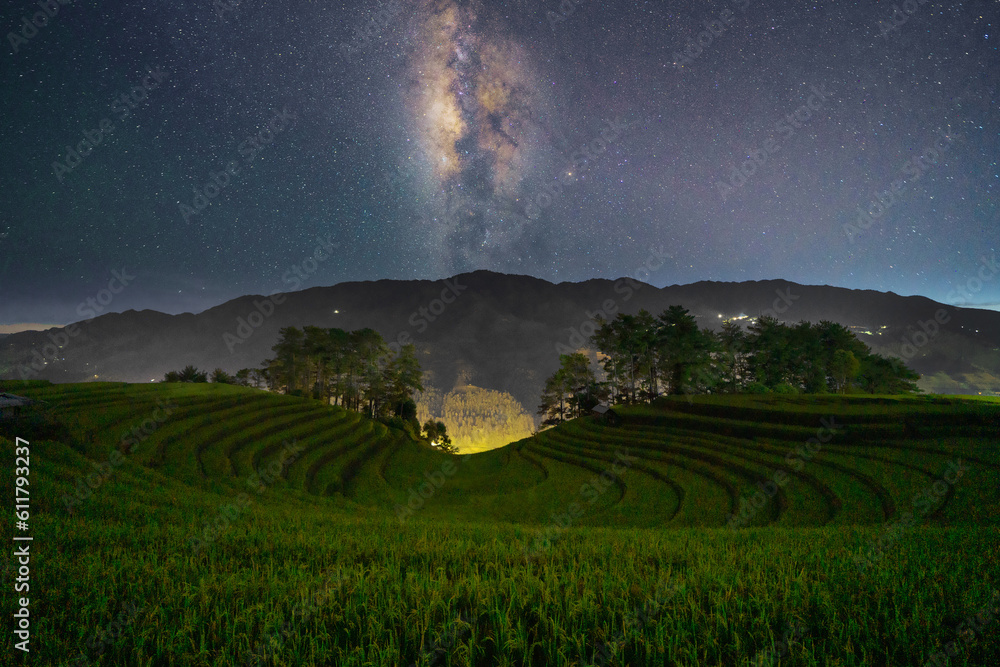 Fresh paddy rice terraces and milky way and stars on space, green agricultural fields in countryside or rural area of Mu Cang Chai, mountain hills valley in Asia, Vietnam. Nature landscape at night.