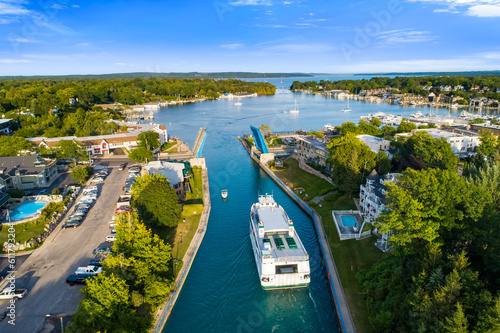 Wallpaper Mural Aerial drone capture of a ferry entering Charlevoix harbor through a raised lift bridge, passing between breakwaters and waterfront buildings, with boats moored along docks under clear blue sky and em Torontodigital.ca