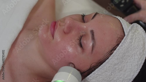 Massaging facial skin of a young woman using a cosmetology device photo