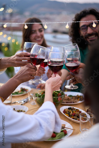 Vertical gathering of young friends toasting with red wine and celebrating party on terrace of house. People together drinking alcoholic beverages outdoor. Boys and girls enjoying free time on weekend #611793627