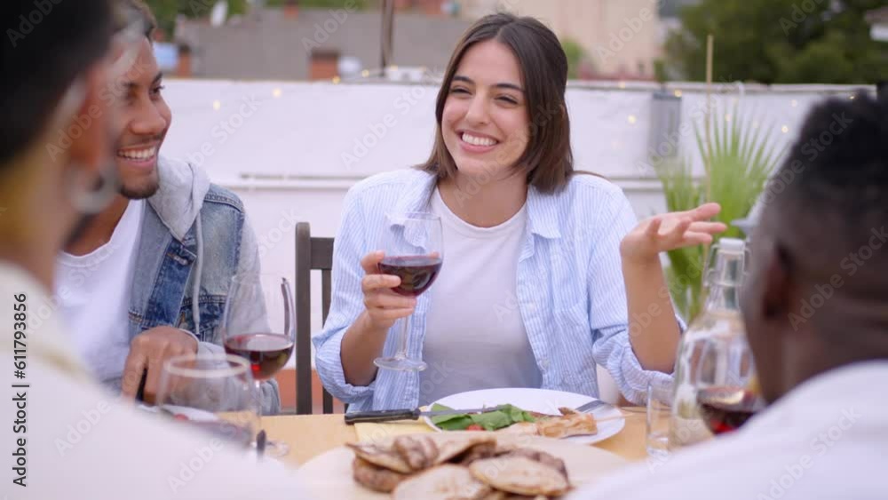Shot of young woman smiling surprised holding glass of wine chatting with friends. People gathered celebrating outdoor barbecue. Slow motion multi-ethnic group having lunch on rooftop on summer day. Shot of young woman smiling surprised holding glass of wine chatting with friends. People gathered celebrating outdoor barbecue. Slow motion multi-ethnic group having lunch on rooftop on summer day.