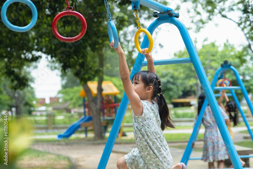 Happy girl hanging on monkey bar by hand doing exercise. Little Asian girl playing at outdoor playground in the park on summer vacation. Healthy activity.