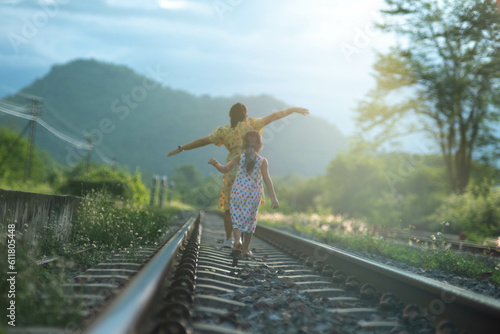 Mother and cute daughter walking on the railroad in the daytime. Happy family walking on the railway against the background of mountains and greenery.