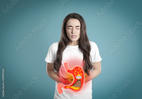 Woman suffering from heartburn on turquoise background. Stomach with erupting volcano symbolizing acid indigestion, illustration photo