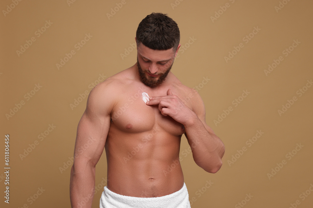 Fototapeta premium Handsome man applying body cream onto his chest on pale brown background