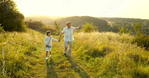 Grandfather and grandson walking at sunset in the field
