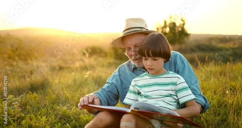 Granfather and grandson laying in grass and reading a book