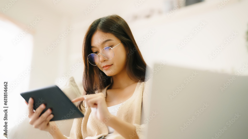 Young asian woman wearing glasses and using tablet while seated on couch at home Young asian woman wearing glasses and using tablet while seated on couch at home