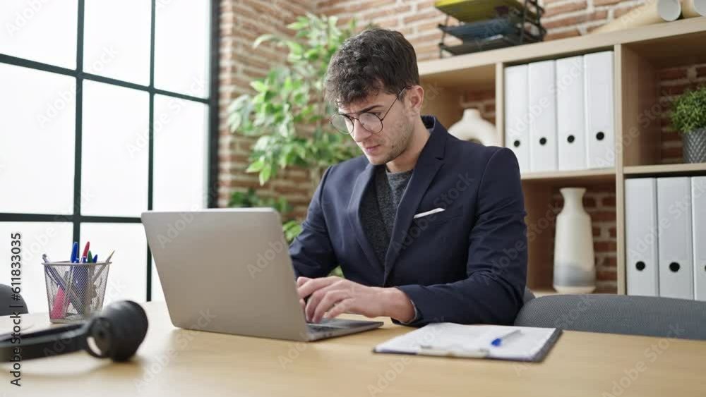 Young hispanic man business worker using laptop writing on clipboard at office Young hispanic man business worker using laptop writing on clipboard at office