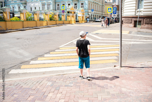 a boy is about to cross the road at a pedestrian crossing alone on a sunny day in the old historic city
