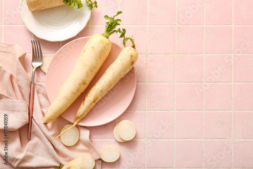 Plates with fresh daikon radishes on pink tile background