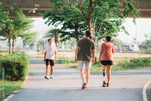 Woman exercising in a park with a friend providing support while using a prosthetic leg. People jogging side by side outside in a park. Female walking and exercise works out outside. photo