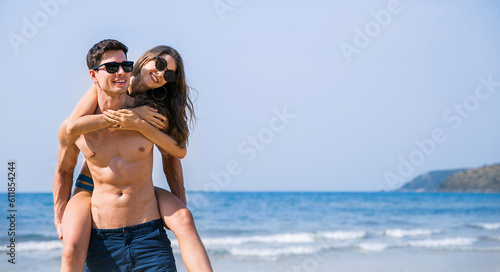 Portrait of beautiful caucasian woman with man wearing sunglasses swim suit piggy back on beach. Young couple enjoy honeymoon after marriage sea. Happy casual lover hold at the tropical beach