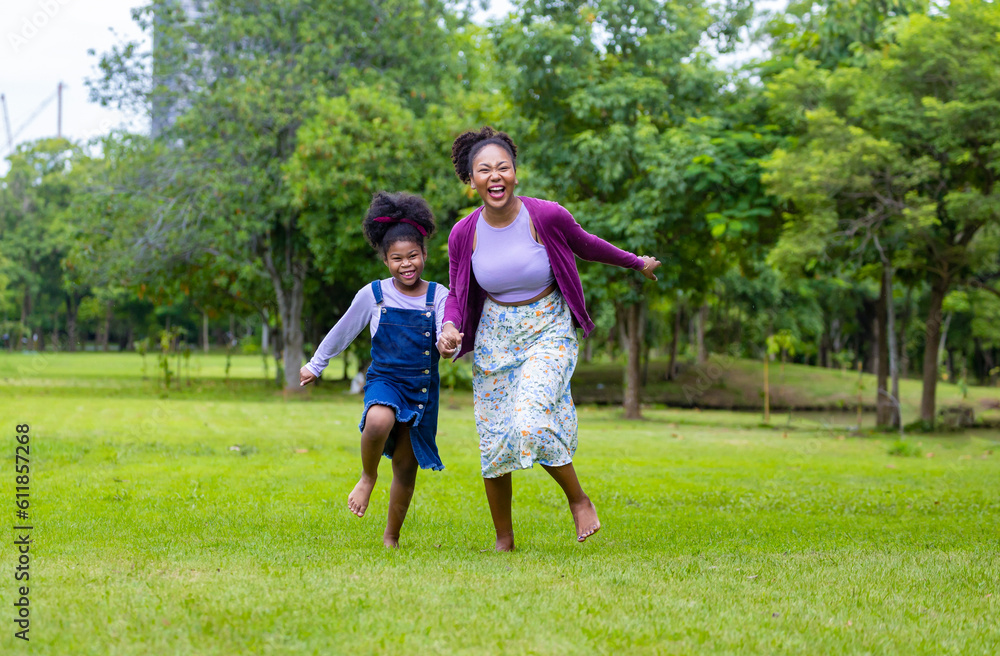 African American mother running barefoot on the grass lawn with her young daughter while having a summer picnic in the public park for wellbeing and happiness African American mother running barefoot on the grass lawn with her young daughter while having a summer picnic in the public park for wellbeing and happiness