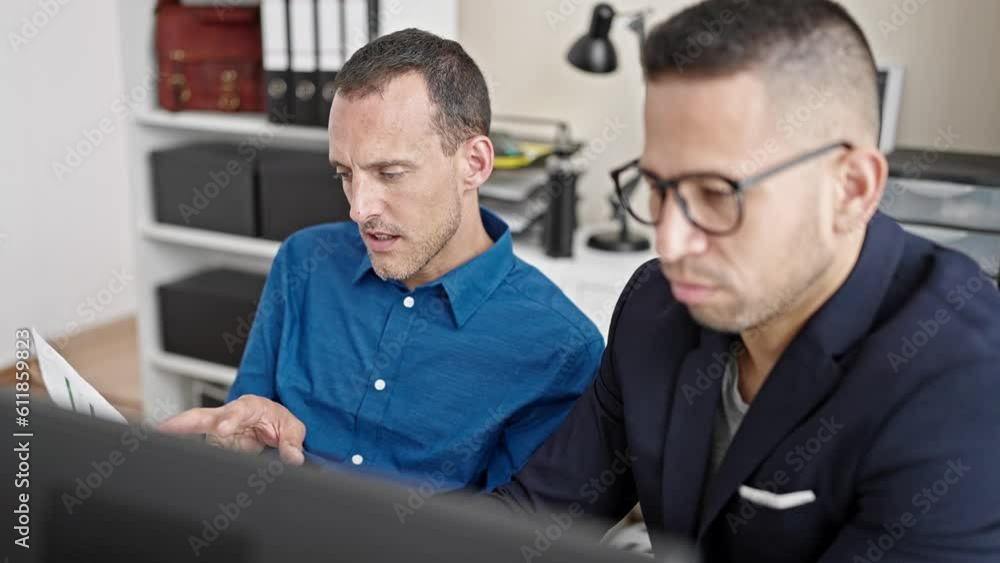 Two men business workers using computer reading document at office Two men business workers using computer reading document at office