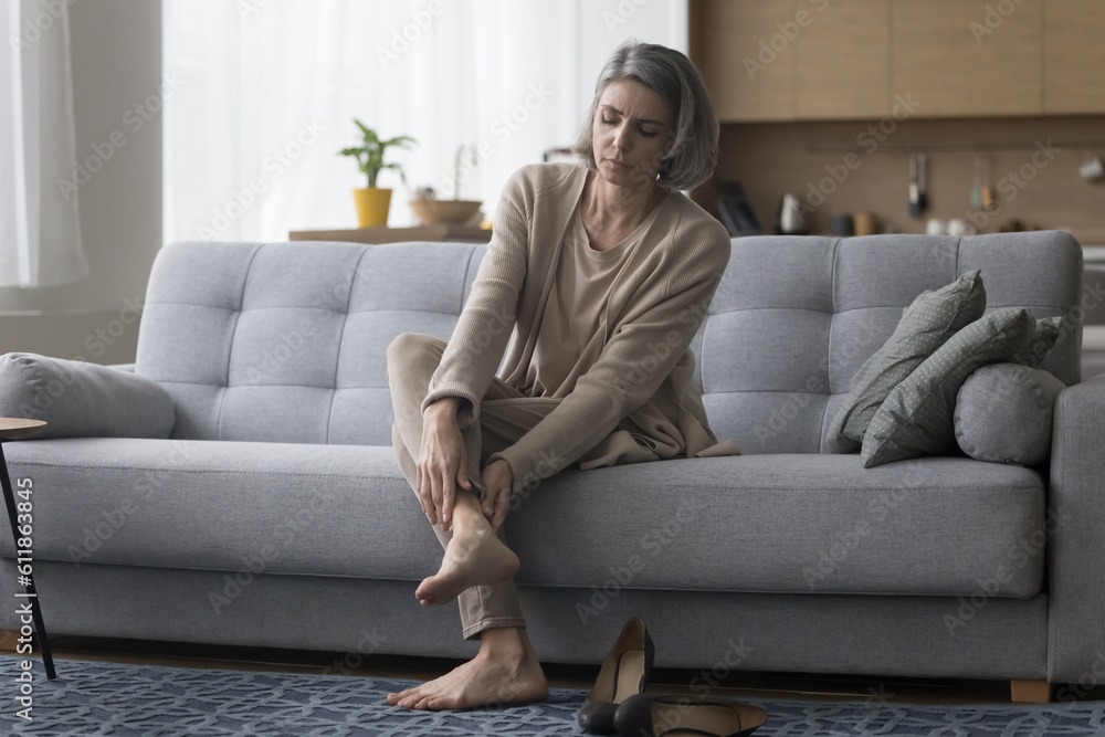Frustrated concerned mature woman taking high heeled shoes off, sitting