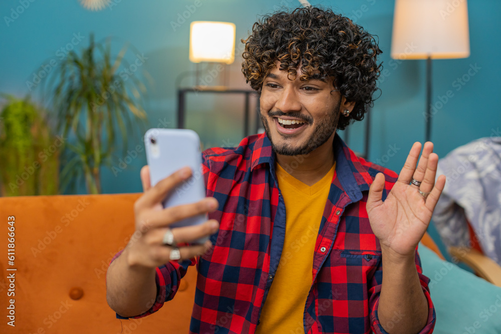 Happy indian man blogger taking selfie on smartphone, communicating video call online with social media subscribers followers, recording vlog stories. Young hindu guy at home apartment room on couch Happy indian man blogger taking selfie on smartphone, communicating video call online with social media subscribers followers, recording vlog stories. Young hindu guy at home apartment room on couch