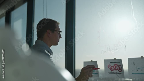 Businessman stands at office window with financial report in hands and marks growth of stocks with marker on glass photo
