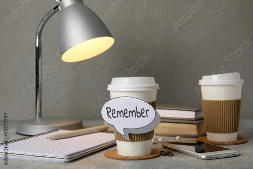 Cup of coffee with reminder, mobile phone, notebooks and glowing lamp on grunge table, closeup photo