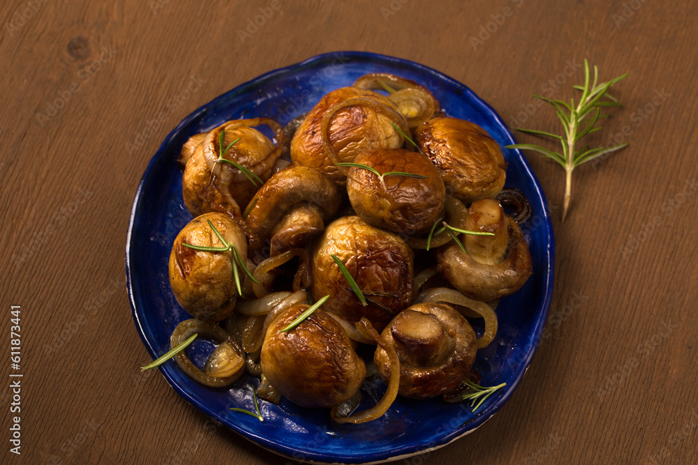 Fototapeta premium Fried mushrooms champignons with rosemary on a plate on a dark background
