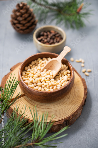 Pine nuts in a bowl on a wooden board on a blue texture background with branches of pine needles and a cone close up. The concept of a natural, organic and healthy superfood
