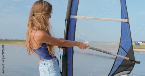 smiling happy fit woman in shorts and swimsuit stands on windsurf and holds the sail. woman windboarder holding sail girl windboarding windsurfing on water extreme sport photo