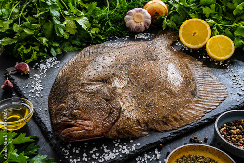 Big raw turbot with fresh vegetables on black stone board