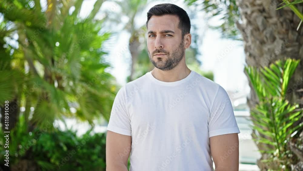Young hispanic man standing with serious expression saying no with head at park
