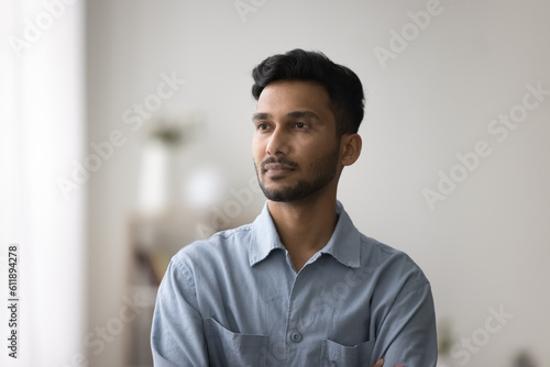Serious thoughtful young Indian man indoor portrait. Pensive dreamy handsome businessman, entrepreneur, Internet startup manager looking at window away, thinking over creative ideas for project
