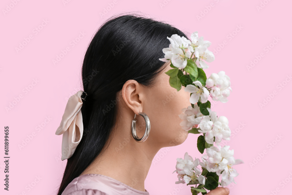Profile of beautiful young woman wearing stylish jewelry with flower near pink wall Profile of beautiful young woman wearing stylish jewelry with flower near pink wall