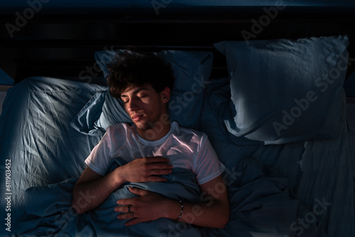 Top view of young man sleeping on a bed in his bedroom at night. Light shining through the window. People, bedtime and rest concept.