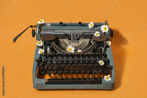 Vintage typewriter with daisy on orange background photo