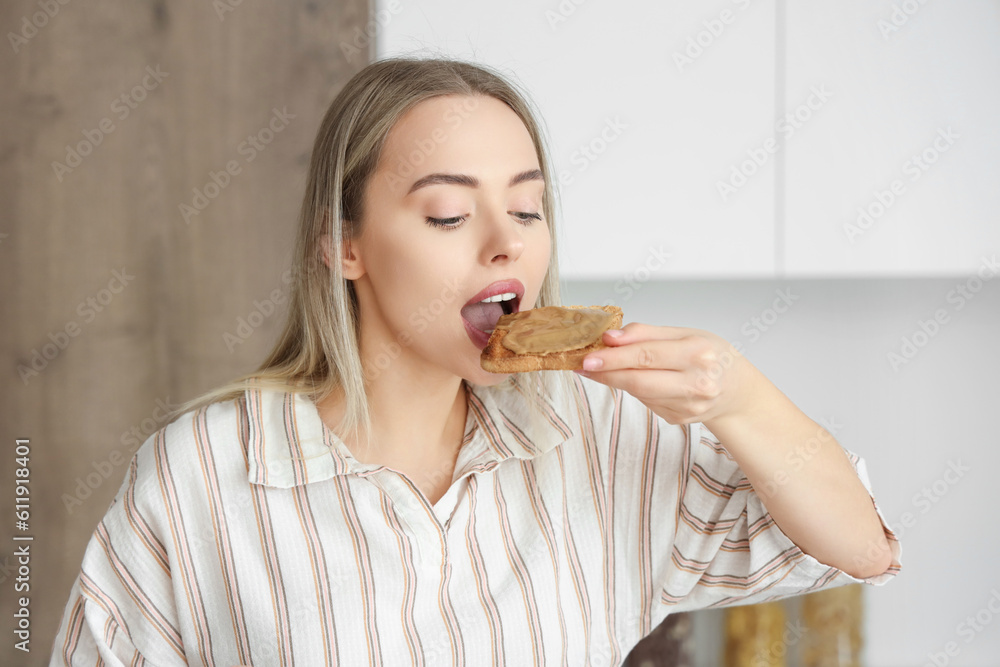 Young woman eating toast with nut butter in kitchen, closeup