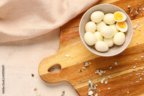 Board with bowl of boiled quail eggs and shells on white wooden background