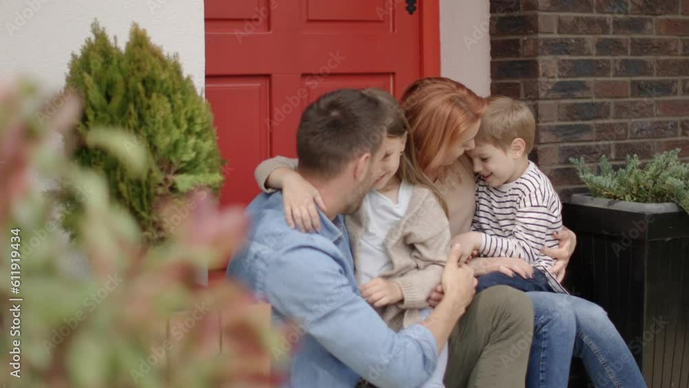 Family with a mother, father, son and daughter sitting outside on steps of a front porch of a brick house Family with a mother, father, son and daughter sitting outside on steps of a front porch of a brick house