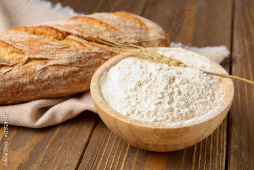 Bowl of wheat flour with fresh bread on brown wooden background