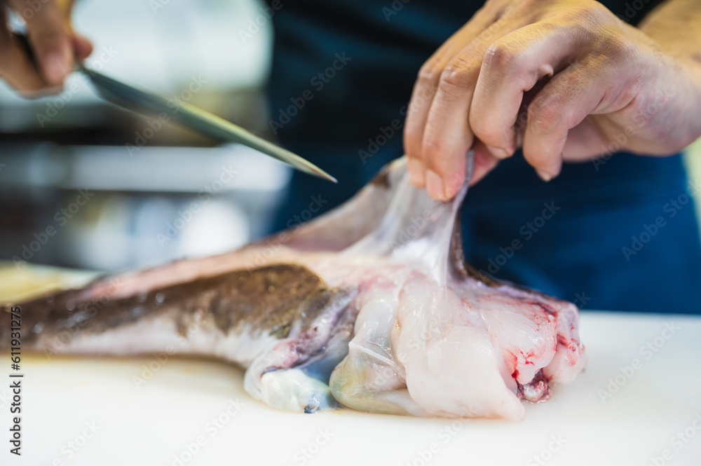 Close-up of a cook's hands cutting angler fish in a restaurant.
